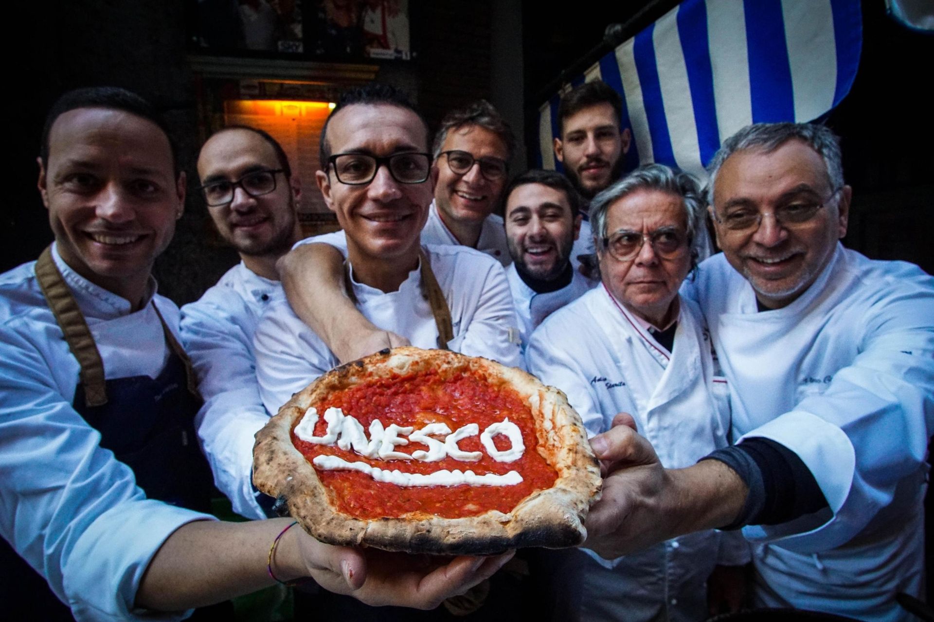 Pizzeros celebran el reconocimiento de la UNESCO mientras posan con una pizza en Nápoles, Italia.