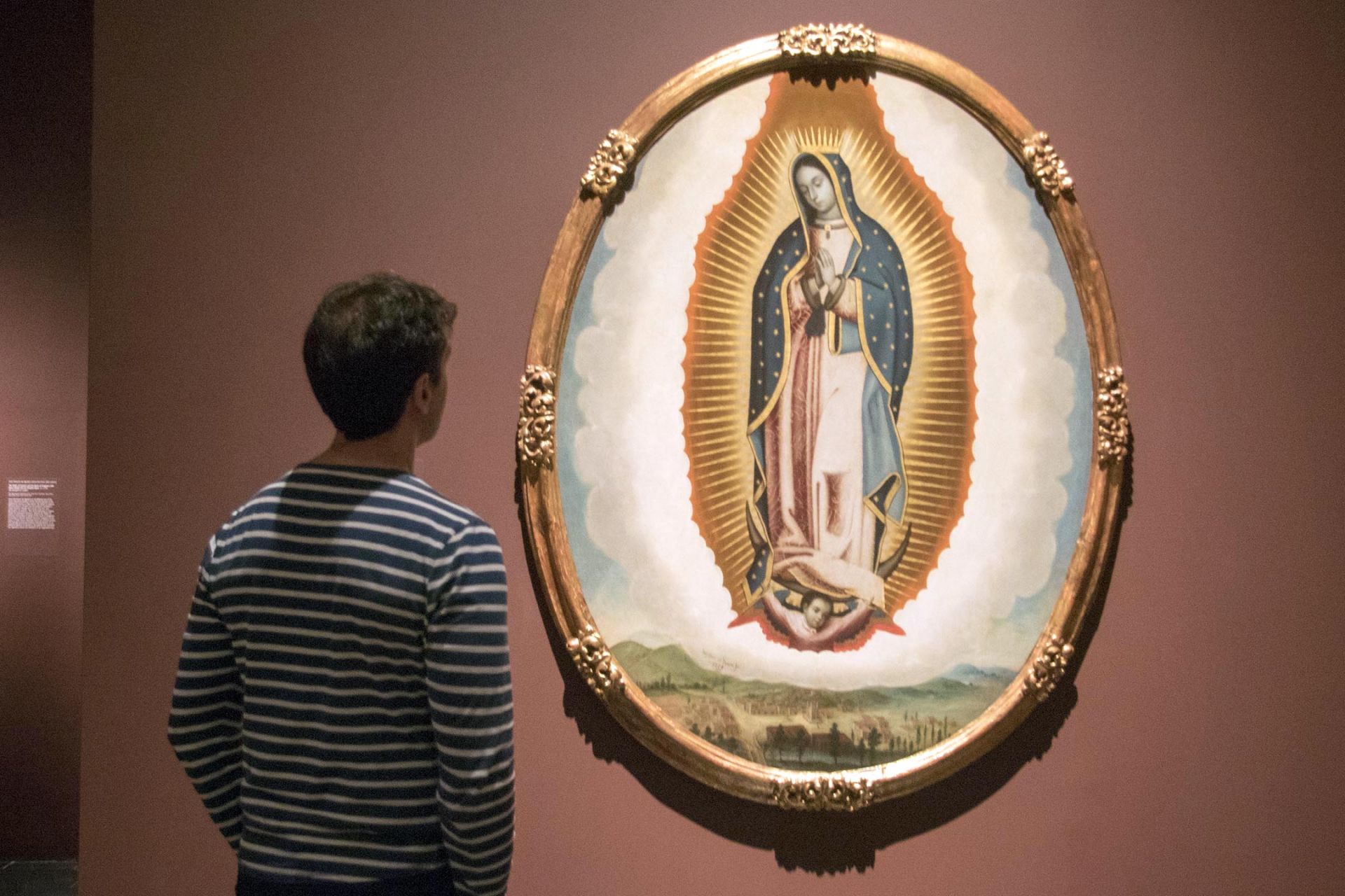 Una persona observa la obra "Virgen de Guadalupe y vista del valle de México" (1739) de José de Ibarra.